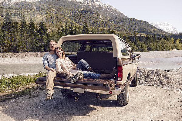 Paar sitzt hinten auf einem Pickup und schaut in die Kamera  Wallgau  Bayern  Deutschland