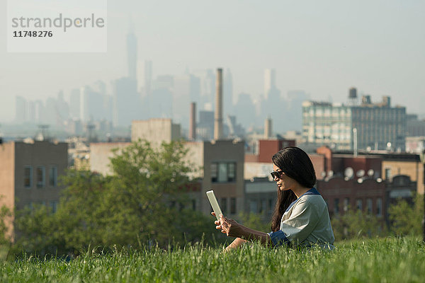 Mittelgroße erwachsene Frauen mit digitalem Tablet im Sunset Park mit der Skyline von Manhattan