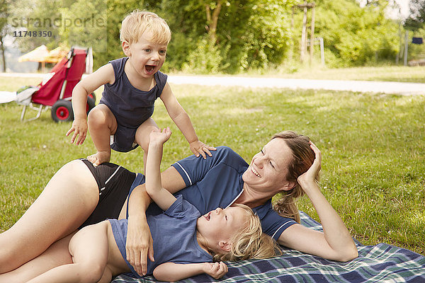 Mutter und Söhne entspannen sich im Park  auf einer Picknickdecke liegend