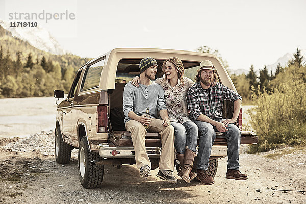 Drei Personen sitzen hinten auf einem Pickup  die Arme um die Schultern gelegt  lächelnd