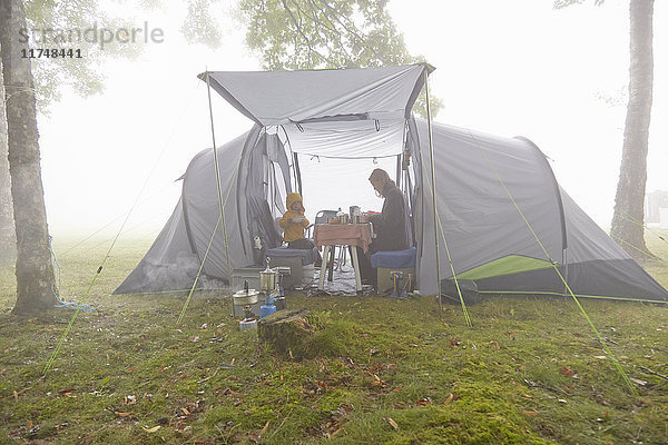 Mutter und Söhne beim Frühstück im Zelt in nebliger Landschaft