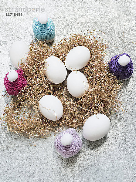 Draufsicht auf Eier mit gehäkelten Knithats auf Strohbett
