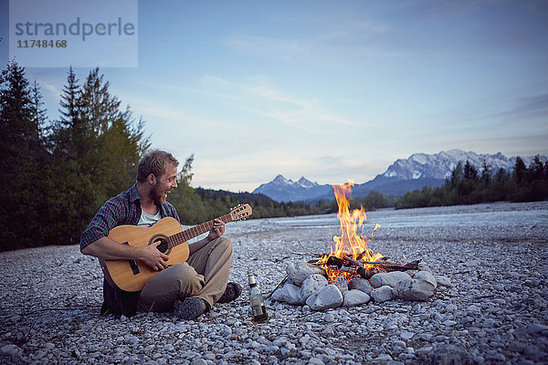 Junger Mann sitzt am Lagerfeuer  spielt Gitarre  singt  Wallgau  Bayern  Deutschland