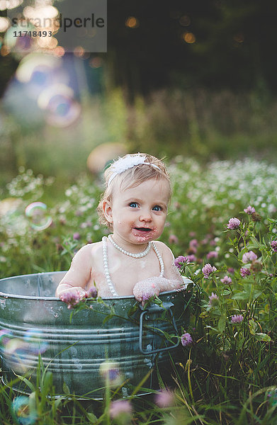 Porträt eines Mädchens  das in einer Blechbadewanne auf einer Wildblumenwiese badet