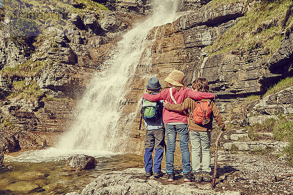 Drei Kinder stehen am Wasserfall  Rückansicht