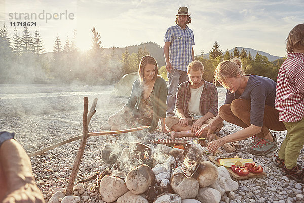 Familie sitzt am Lagerfeuer und bereitet Essen vor