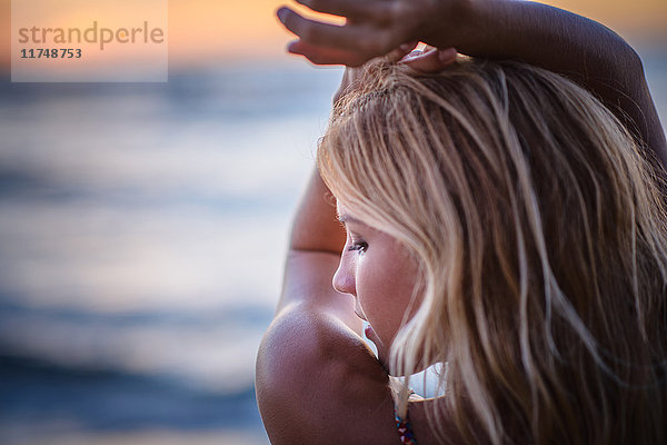 Junge Frau mit erhobenen Armen bei Sonnenuntergang am Strand