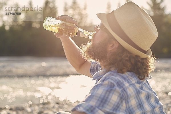 Seitenansicht eines mittleren erwachsenen Mannes mit Hut  der Bier aus einer Bierflasche trinkt