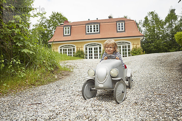 Junge spielt mit Oldtimer-Spielzeugauto auf der Auffahrt vor dem Haus