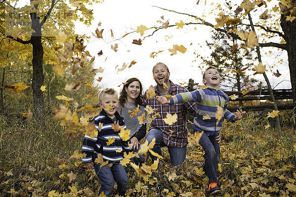 Frontansicht einer Familie  die das Herbstlaub tritt und lächelnd in die Kamera schaut