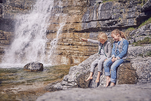Bruder und Schwester  auf einem Felsen sitzend  entspannend  neben einem Wasserfall