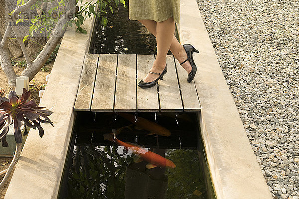 Beine einer mittel-erwachsenen Frau am Fischteich im Garten