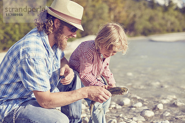 Mittelgroßer erwachsener Mann und Junge neben dem Fluss bei der Untersuchung von Fischen  die an der Angelschnur befestigt sind