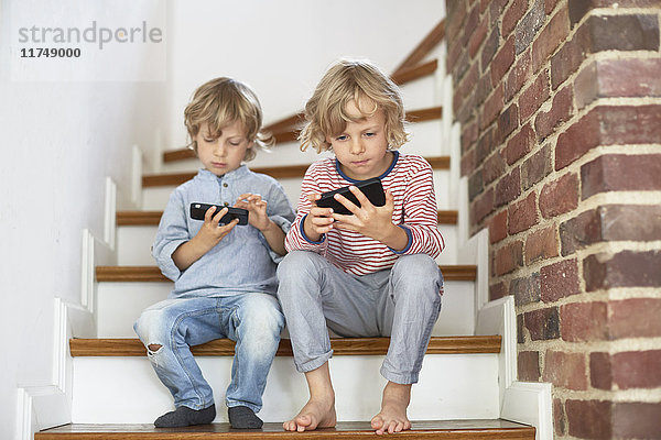 Zwei junge Brüder sitzen auf einer Treppe und schauen auf Smartphones