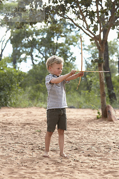 Junge auf Sand mit selbstgemachtem Pfeil und Bogen