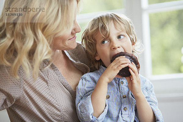Kleiner Junge sitzt auf einem Schokoladenmuffin  während seine Mutter zuschaut