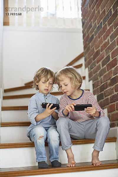 Zwei Jungen  die auf einer Treppe sitzen und auf Smartphones schauen