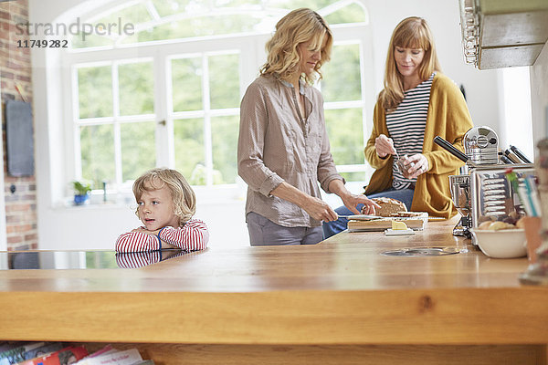 Zwei mittelgroße erwachsene Frauen bereiten das Essen in der Küche zu  während ein Junge an der Küchentheke wartet