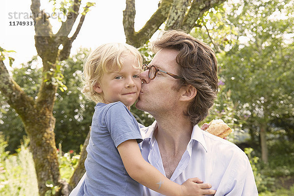Porträt eines reifen Mannes  der seinen Sohn im Garten auf die Wange küsst