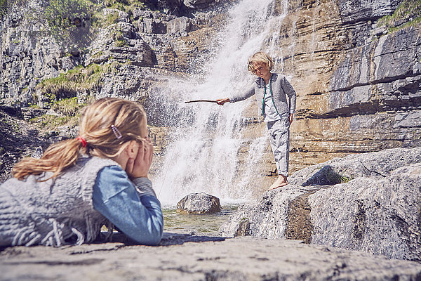 Junges Mädchen beobachtet Bruder  steht neben Wasserfall
