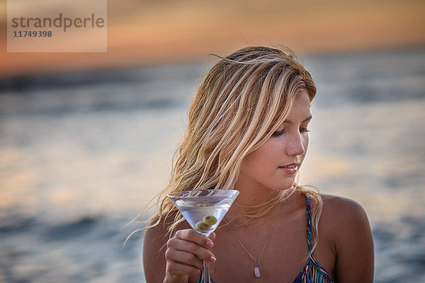 Junge Frau trinkt Cocktail am Strand bei Sonnenuntergang