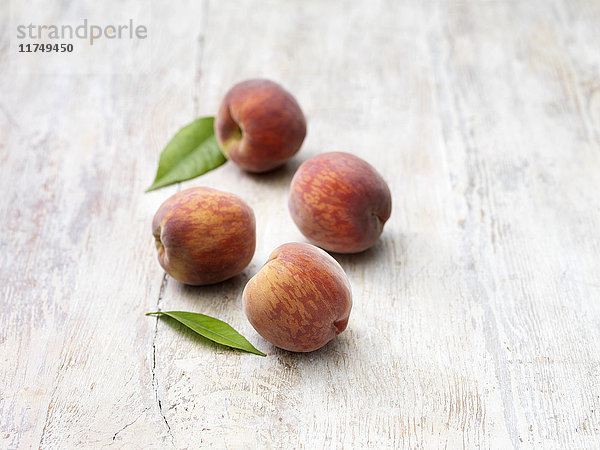 Vier Pfirsiche auf weißgekalktem Holztisch