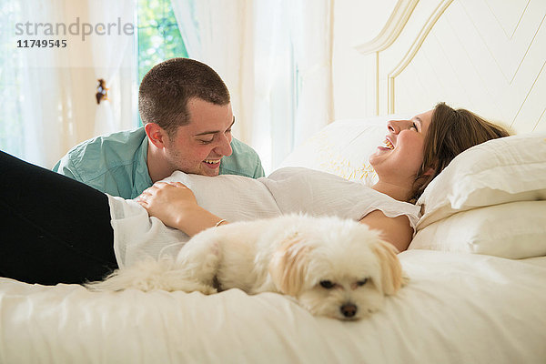 Schwangere Frau und Partner mit Hund im Bett liegend