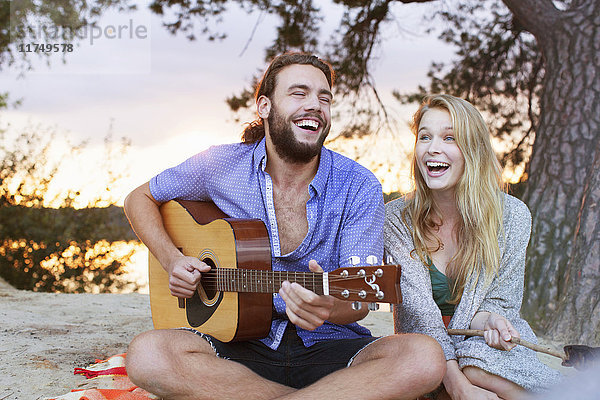 Junges Paar spielt Gitarre am See