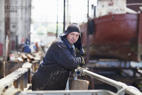 Porträt eines Arbeiters  der sich in einer Werftwerkstatt an ein Geländer lehnt