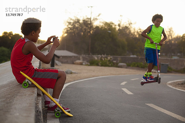 Junge fotografiert Bruder beim Roller-Sprung auf Straße