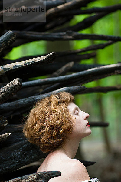 Nahaufnahme einer Frau im Wald vor einem Holzstapel