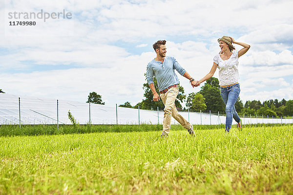 Junges Paar hält sich an den Händen  läuft durch das Feld  neben dem Solarpark