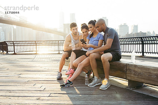 Vier erwachsene  rennende Freunde lesen Smartphone-Text vor der Brooklyn Bridge  New York  USA