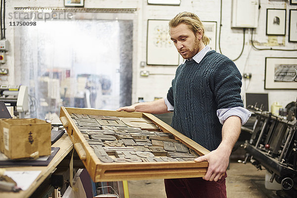 Junger Mann mit Buchdruckschale in traditioneller Druckwerkstatt