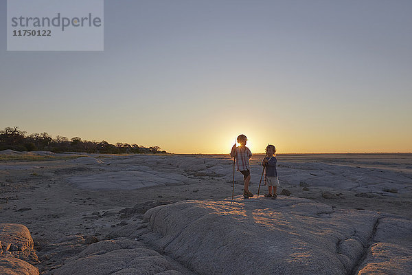 Zwei Jungen stehen auf einem Felsen und halten einen Speer  Sonnenuntergang  Gweta  makgadikgadi  Botswana