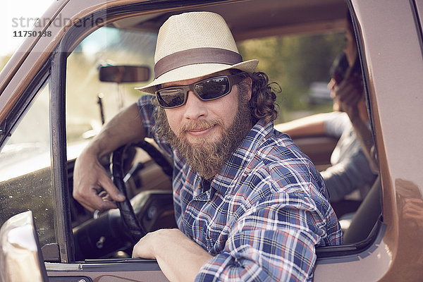 Mittelgroßer erwachsener Mann  der sich mit Sonnenbrille und Hut aus dem Fahrzeugfenster lehnt