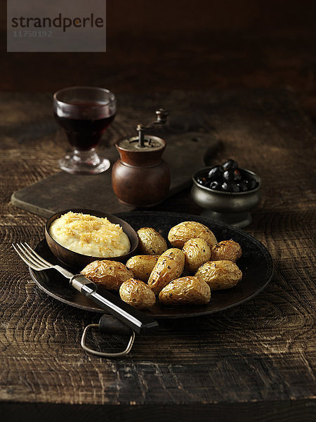 Röstkartoffeln mit einer Schüssel Parmesan-Fondue auf rustikalem Teller