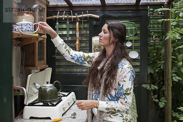 Junge Frau bereitet in offener Hüttenküche Tee zu