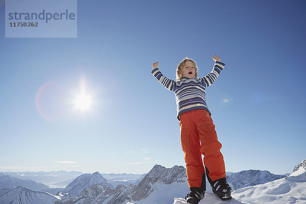 Junge steht in verschneiter Landschaft  feiert mit erhobenen Armen und niedrigem Blickwinkel