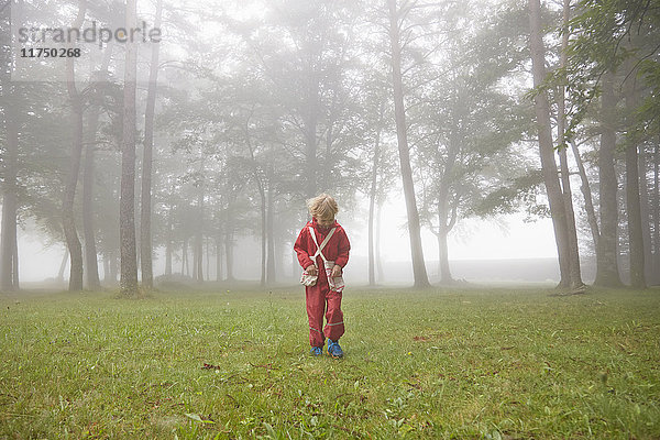 Junge mit roter Regenjacke sucht in nebliger Landschaft