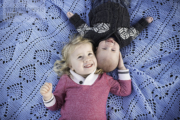Kopfporträt eines Mädchens auf blauer Picknickdecke mit kleinem Bruder