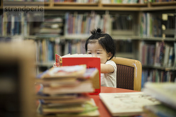 Ein Jahr altes Mädchen liest Buch in der Bibliothek