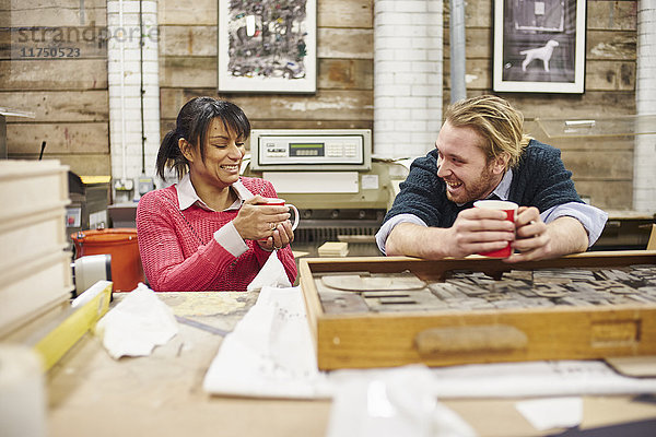 Drucker und Druckerinnen plaudern und trinken Kaffee in traditioneller Druckwerkstatt