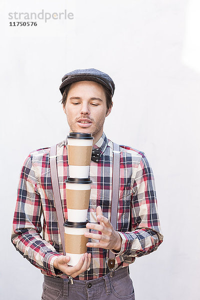 Junger Mann mit geschlossenen Augen trägt drei Kaffees zum Mitnehmen