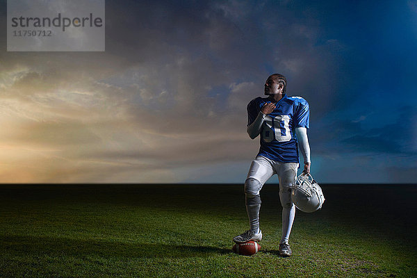 Porträt eines American-Football-Spielers  der mit dem Fuß auf dem Ball ruht