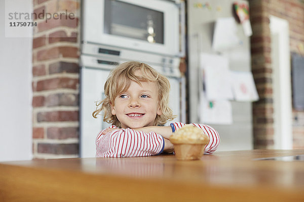 Junge steht an der Küchentheke  vor ihm ein Muffin auf dem Tresen