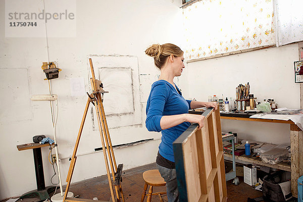 Mittlere erwachsene Frau trägt ein Ölgemälde im Atelier eines Künstlers