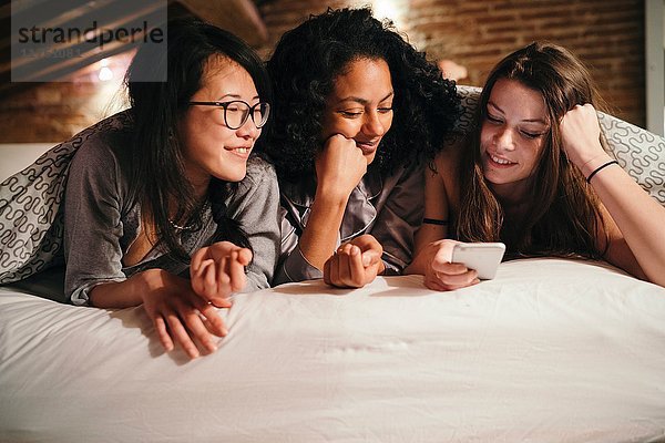 Freunde liegen im Bett und schauen auf das Smartphone