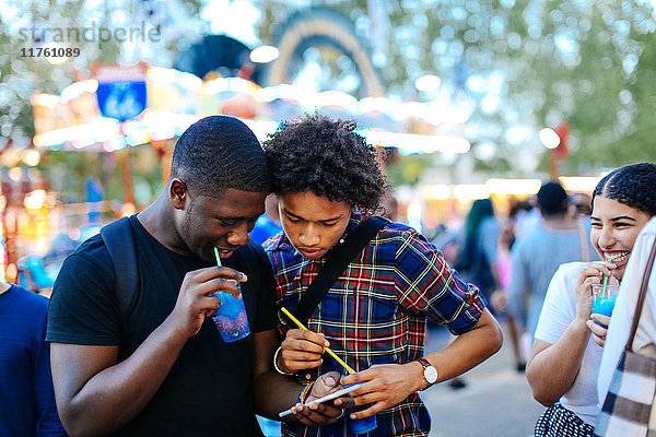 Gruppe von Freunden auf dem Jahrmarkt  zwei Jungen schauen sich ein Smartphone an