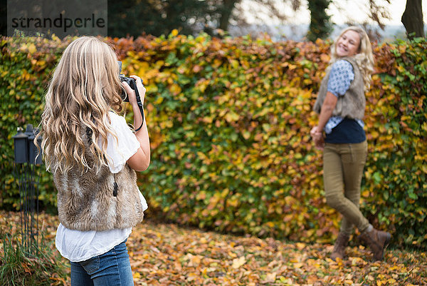 Mädchen fotografiert Schwester an herbstlicher Gartenhecke